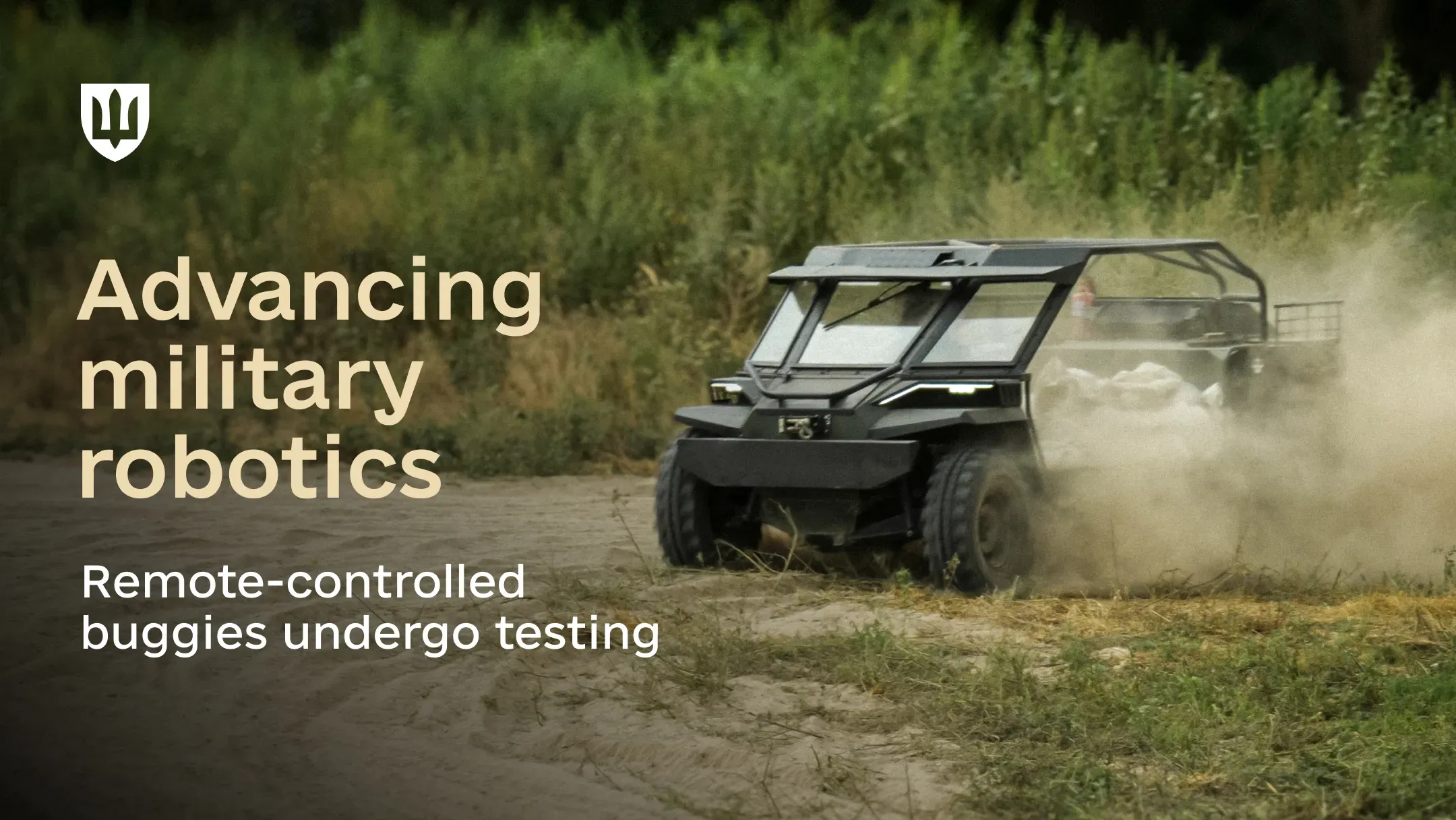 A dark remote-controlled buggy driving along an unpaved field road, kicking up dust against a backdrop of green shrubs