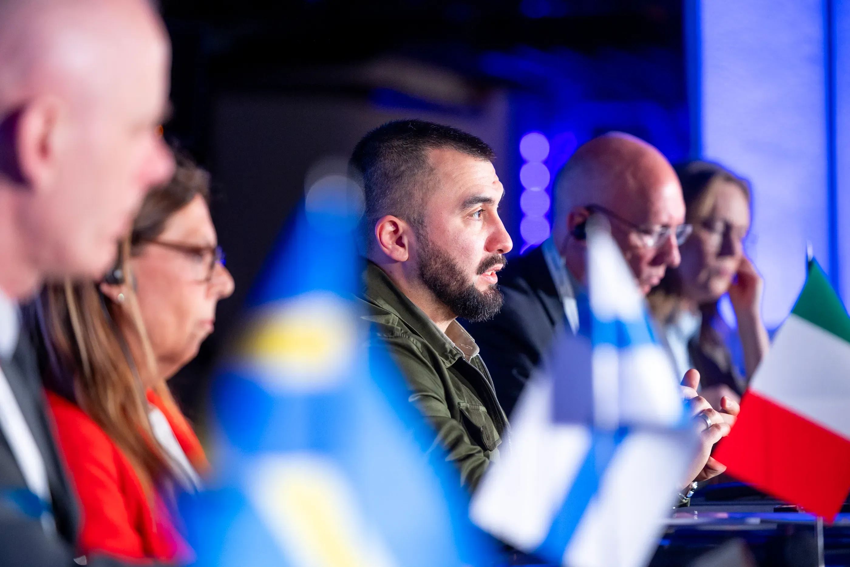 Група людей сидить за столом. Біля них прапорці Швеції, Фінляндії та Італії