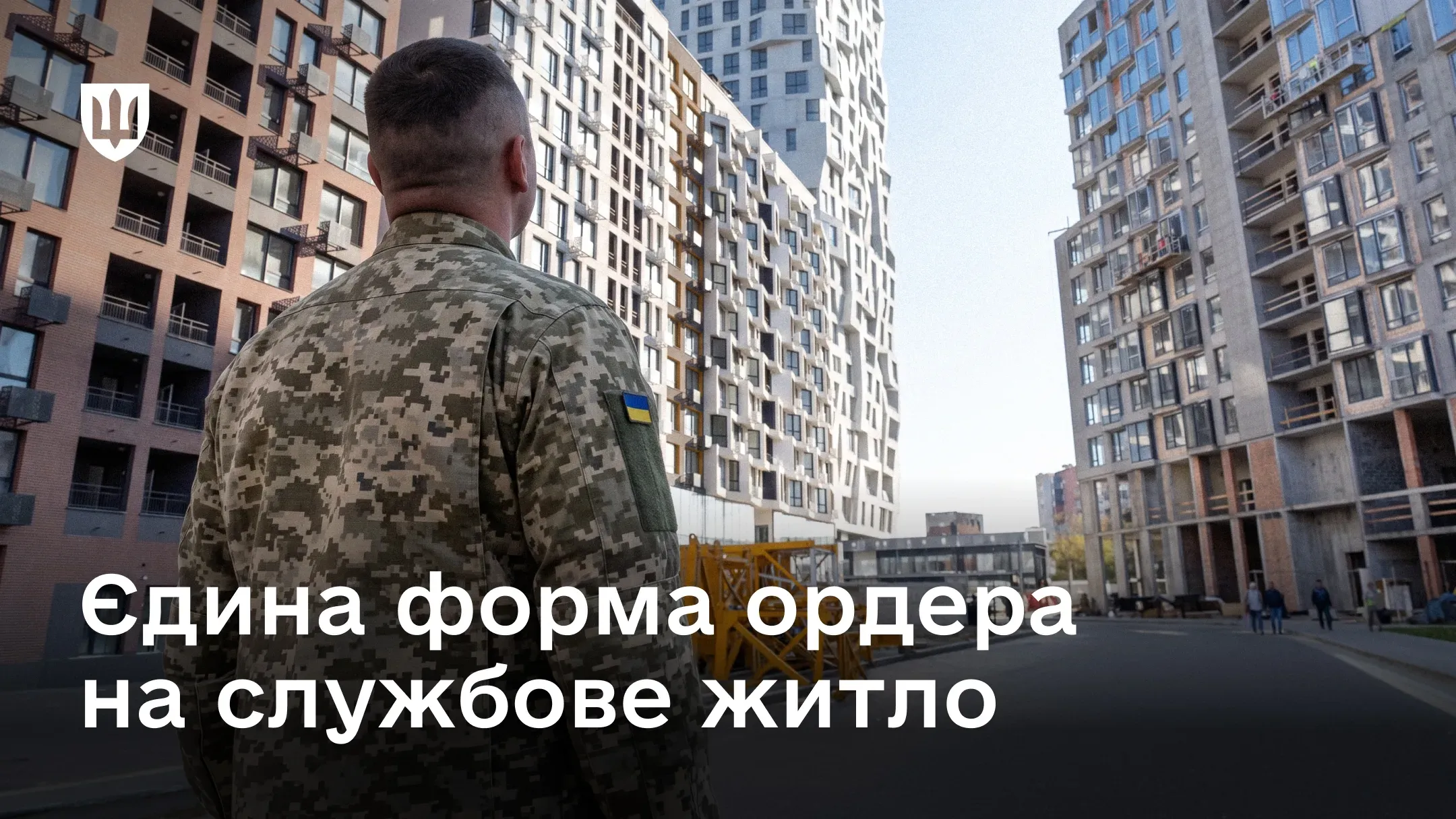 Український військовослужбовець стоїть спиною до глядача і дивиться на сучасні багатоповерхові новобудови.