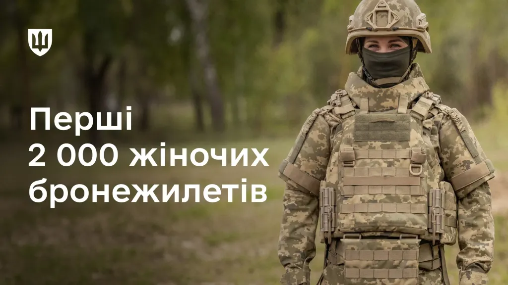 Українська військовослужбовиця у повному екіпіруванні та спеціальному бронежилеті стоїть на тлі дерев