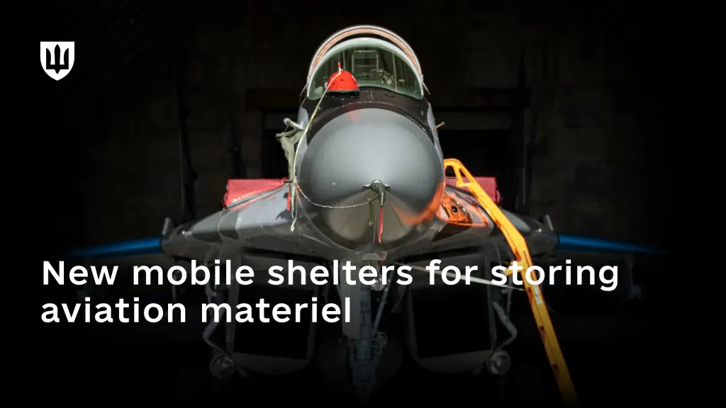 Front view of a military aircraft inside a dark hangar.