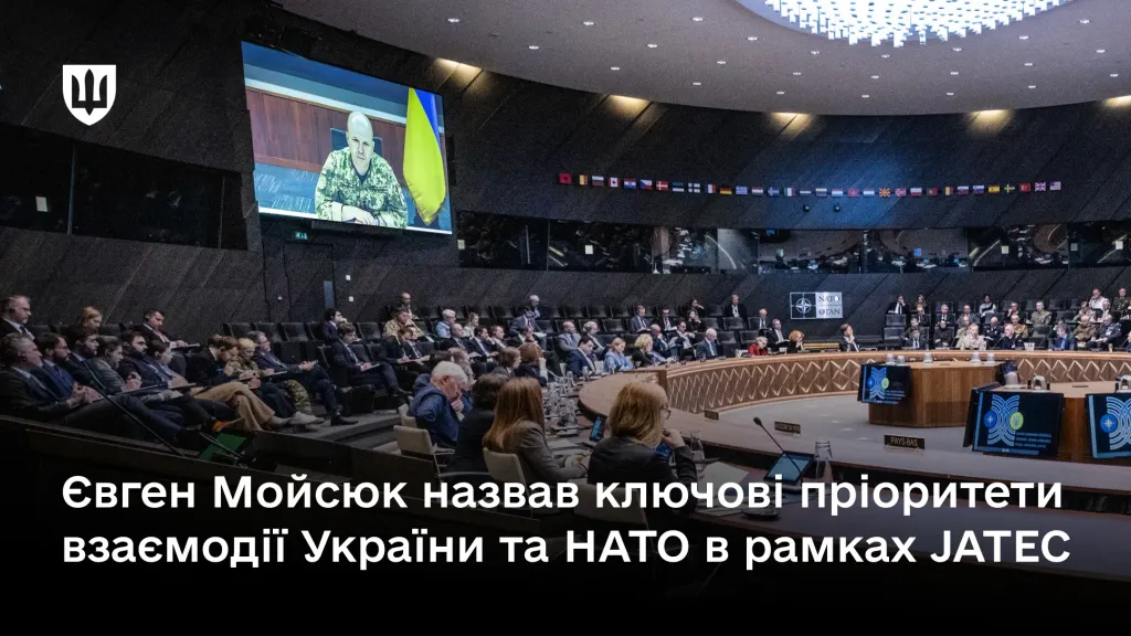 Велика конференц-зала круглої форми, в якій відбувається нарада. З великого екрану виступає заступник Міністра оборони України генерал-лейтенант Євген Мойсюк в піксельній формі
