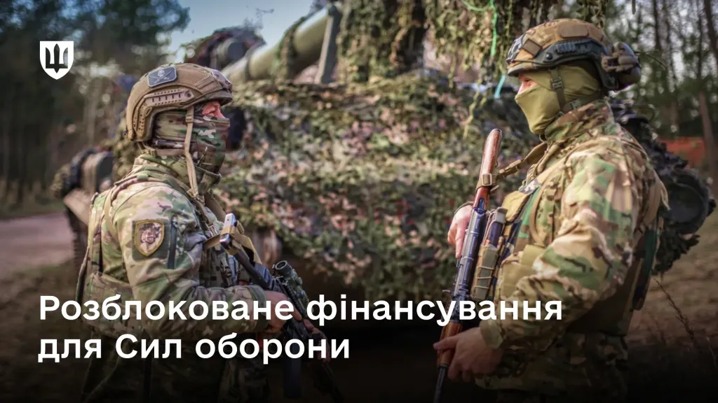 Двоє українських військовослужбовців спілкуються біля замаскованої бронетехніки в лісовій місцевості