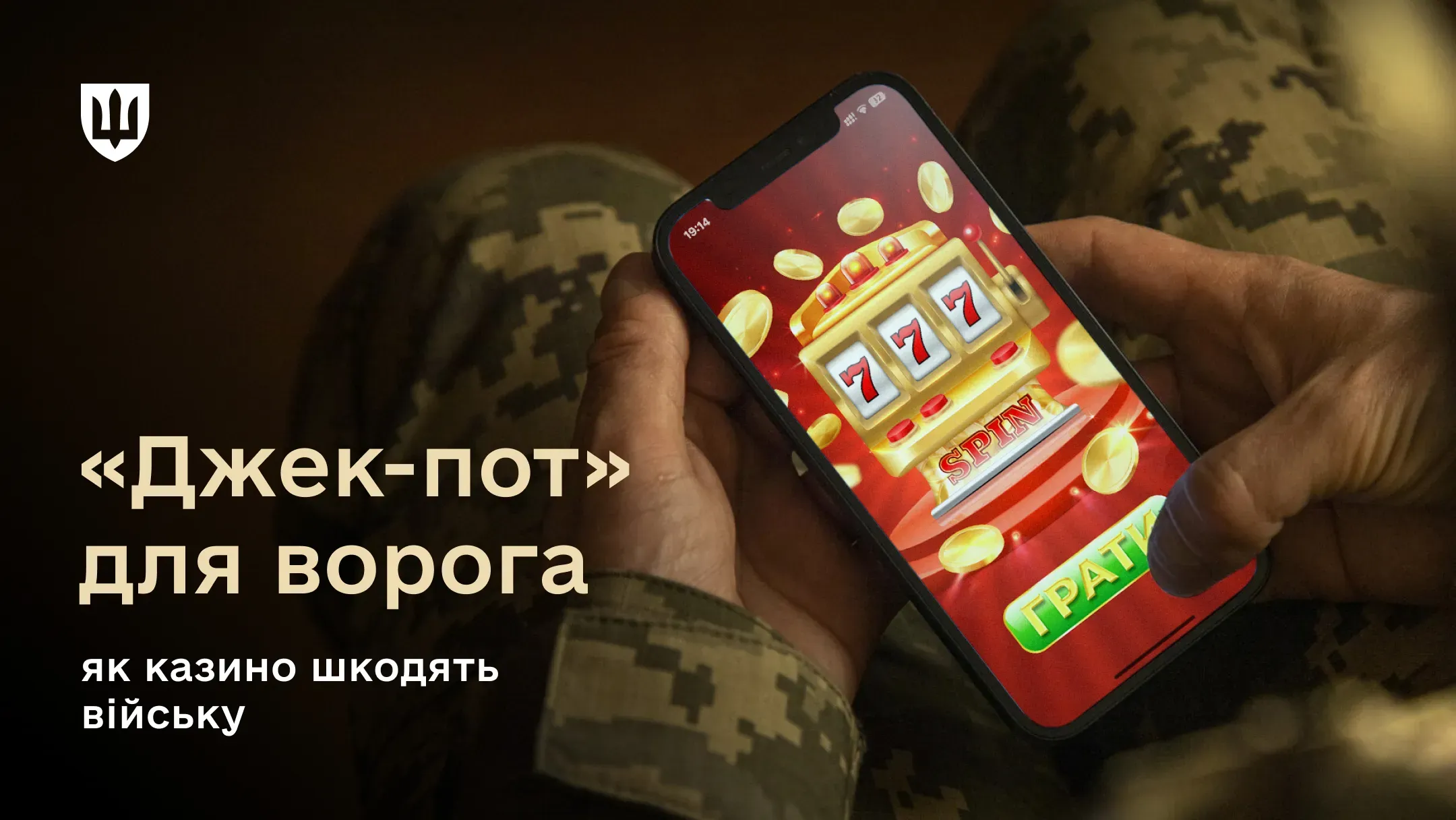 Зображення рук у військовій формі, які тримають смартфон. На екрані смартфона яскраво світиться гра в онлайн-казино — ігровий автомат із сімками та золотими монетами.