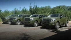Чотири нових пікапи кольору хакі стоять на грунтовій дорозі на фоні лісу