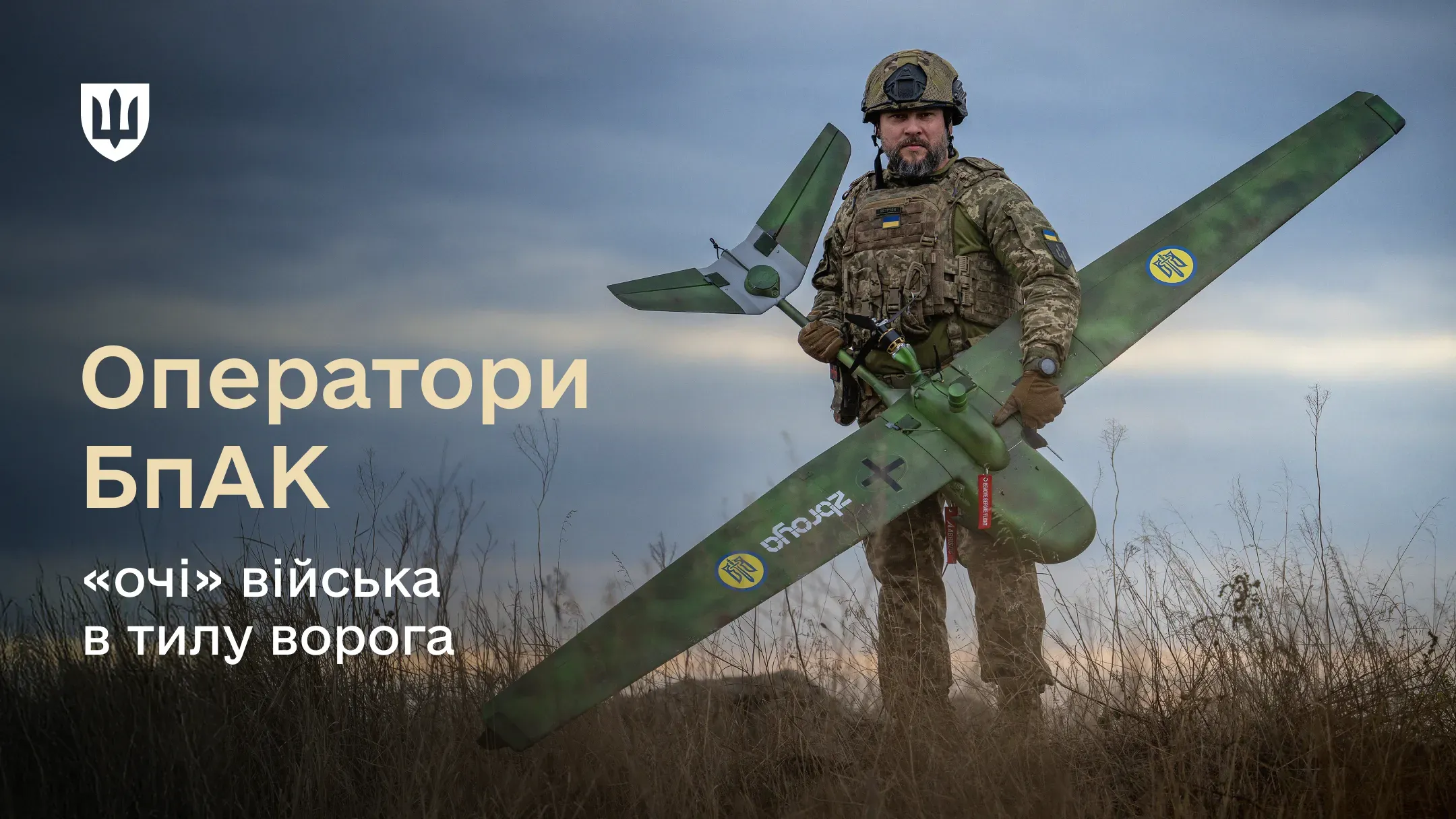 Військовослужбовець ЗСУ в повному бойовому екіпіруванні стоїть у полі та тримає в руках габаритний розвідувальний безпілотник літакового типу