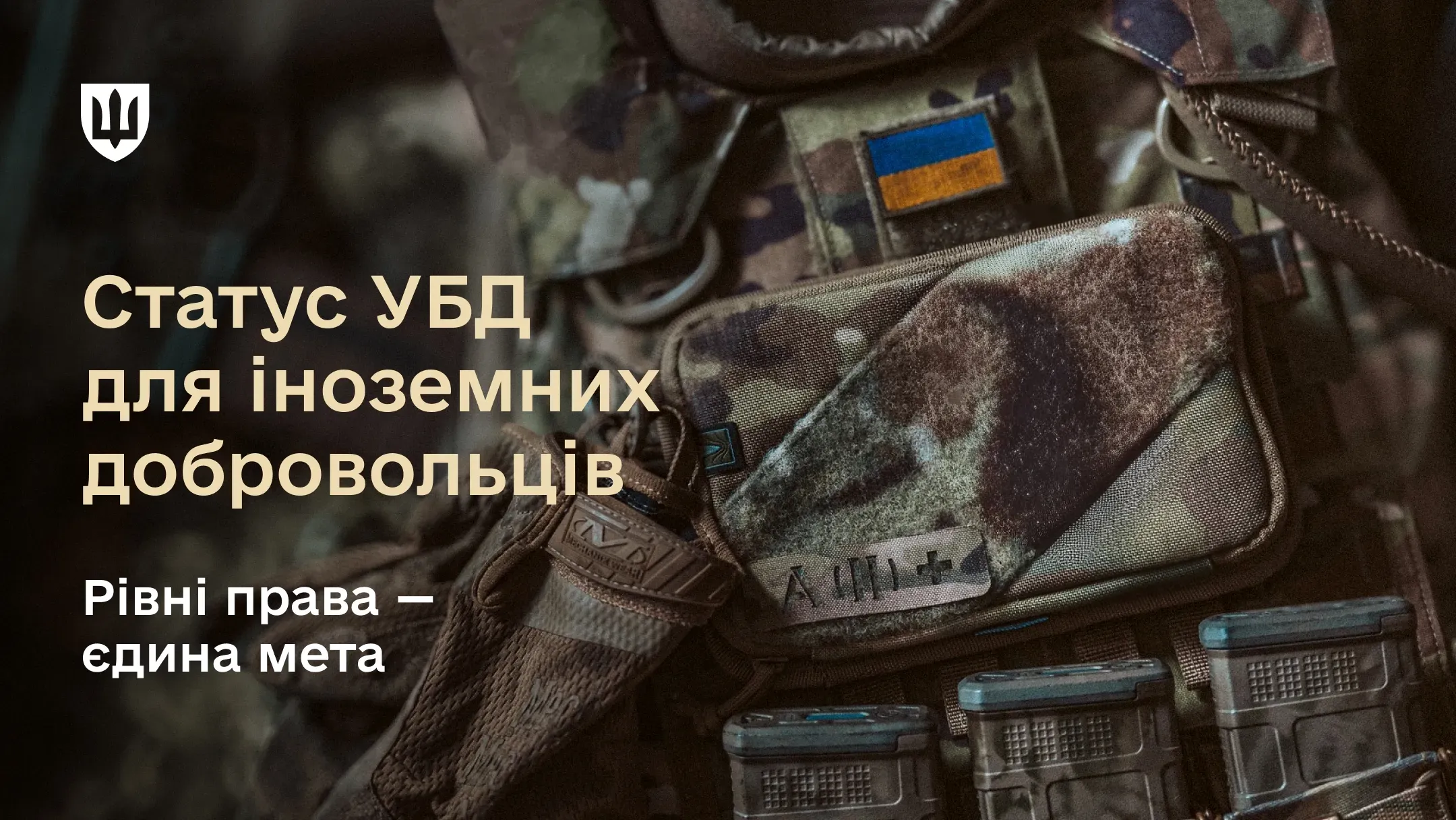 Крупний план військового спорядження з магазинами для зброї та шевронами, поверх якого розміщено текст: "Статус УБД для іноземних добровольців. Рівні права — єдина мета" та логотип Міноборони