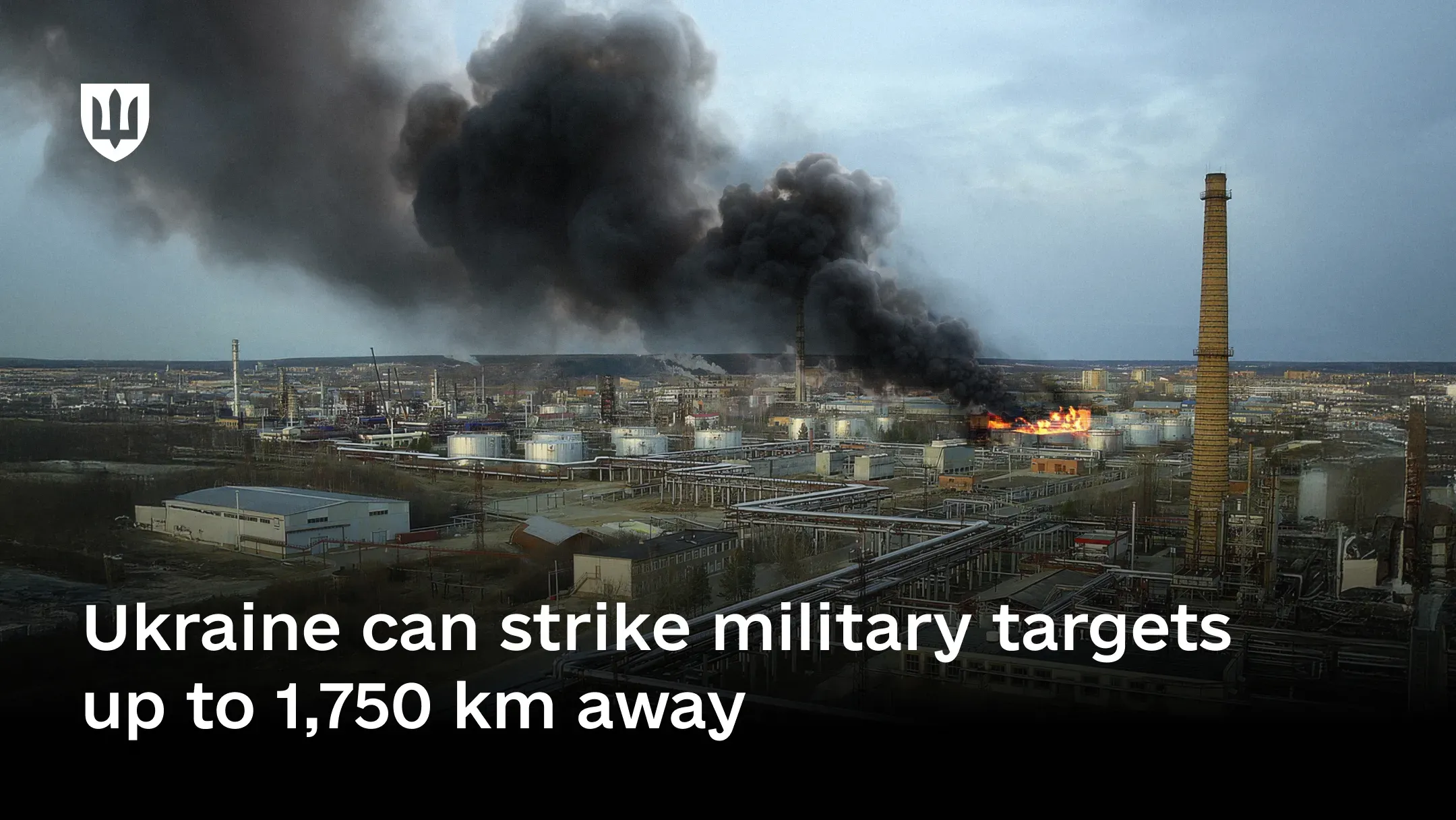 Panoramic view of an oil refinery with a fire and thick black smoke rising over the facility