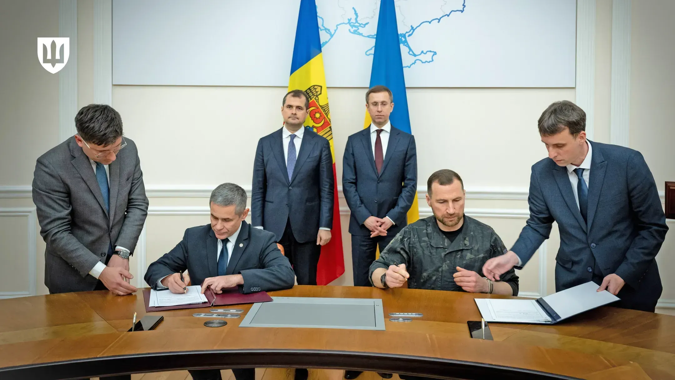The defence ministers of Ukraine and Moldova sign an agreement at a table, with the flags of Moldova and Ukraine behind them