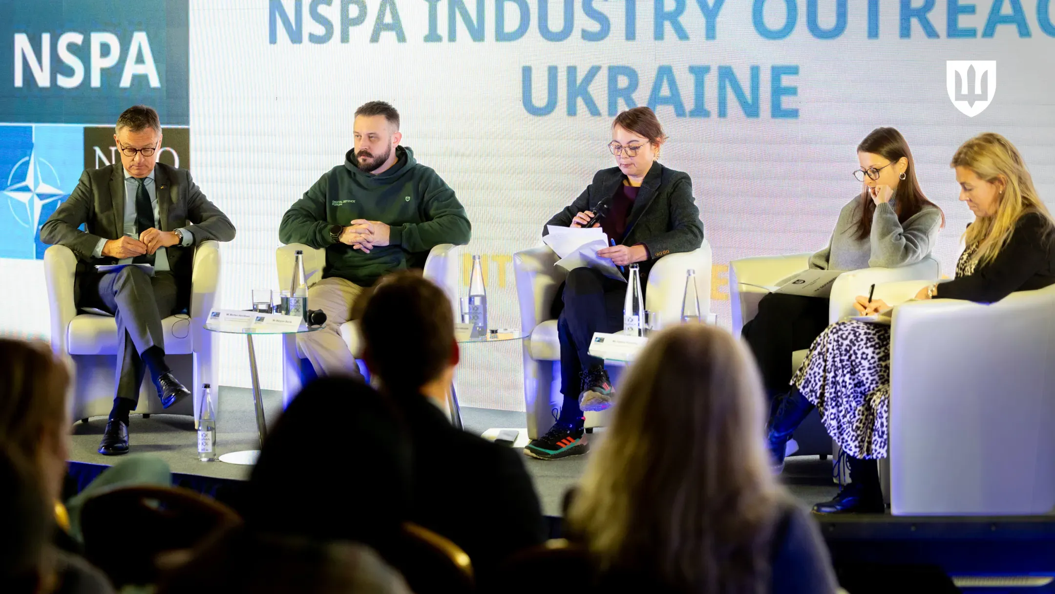 Учасники зустрічі сидять у кріслах на сцені на тлі напису «NSPA INDUSTRY OUTREACH UKRAINE»