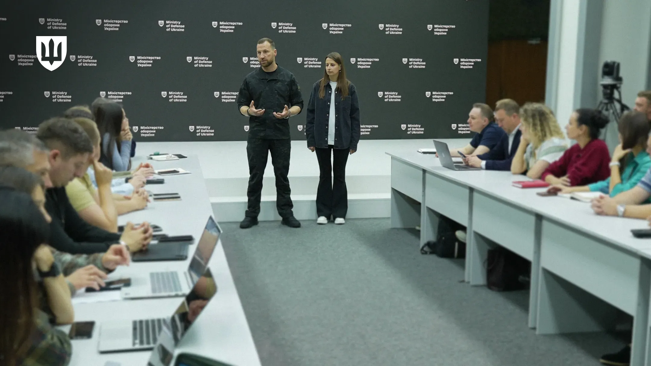 Євгеній Хмара та Ганна Гвоздяр стоять поруч під час зустрічі з представниками українських оборонних підприємств та асоціацій, які сидять за столами