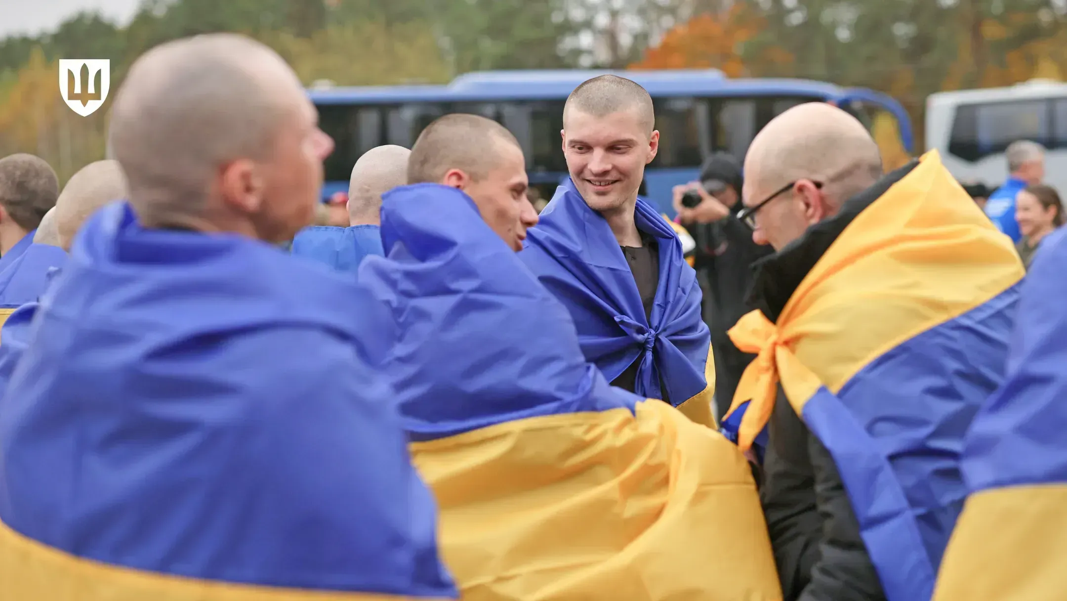Ukrainian service members draped in Ukrainian flags talk and smile after returning from russian captivity
