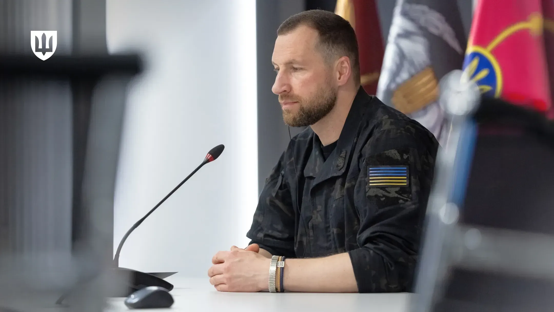Evgeniy Khmara sits at a table with a microphone during a call with his Romanian counterpart, with military flags behind him