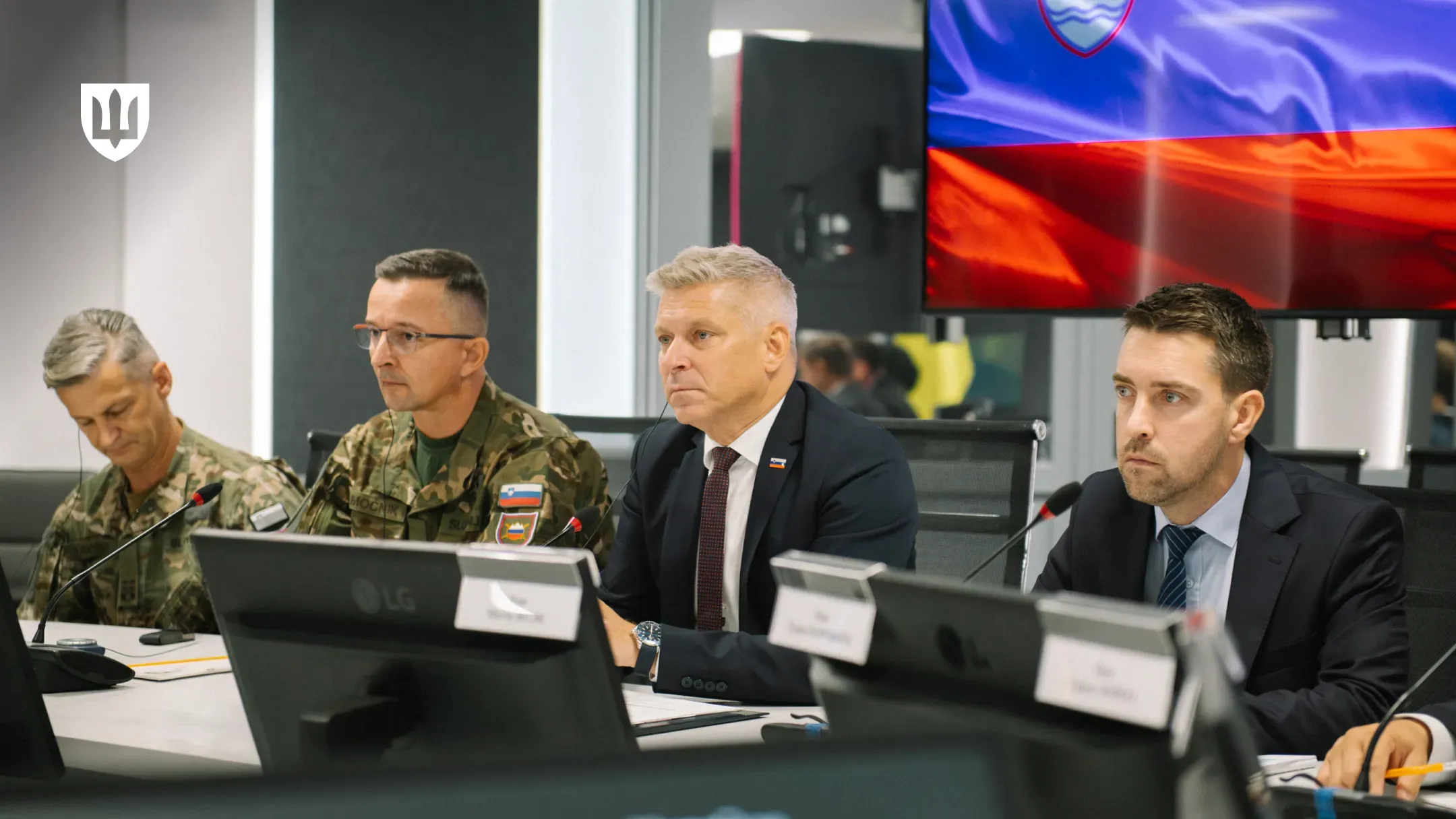 The Slovenian delegation seated at the negotiating table in front of monitors and microphones, with a screen displaying the Slovenian flag in the background