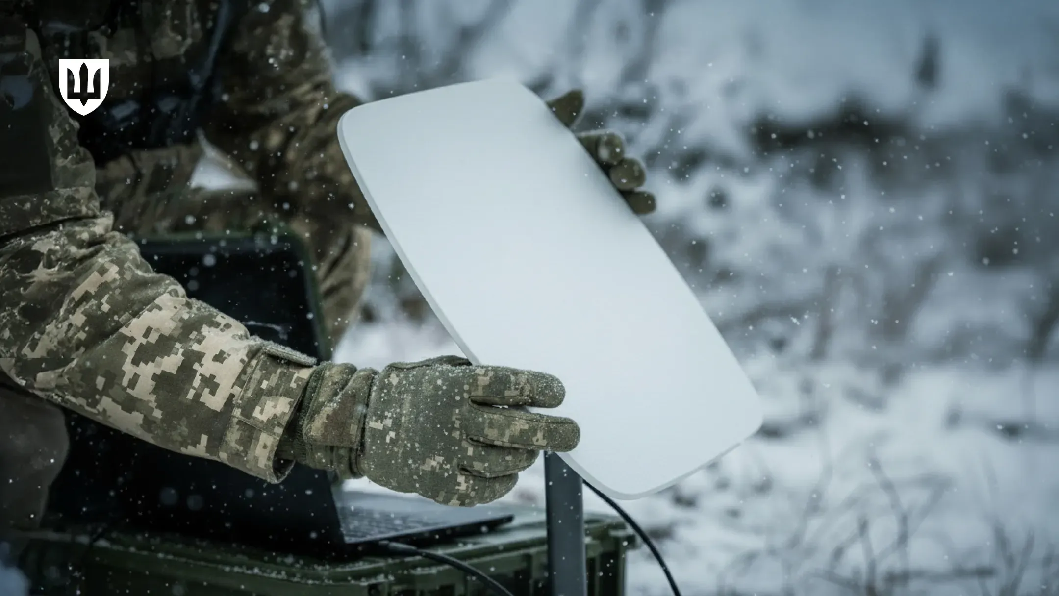 A Ukrainian service member holds a Starlink terminal in winter conditions while setting up connectivity at a position.