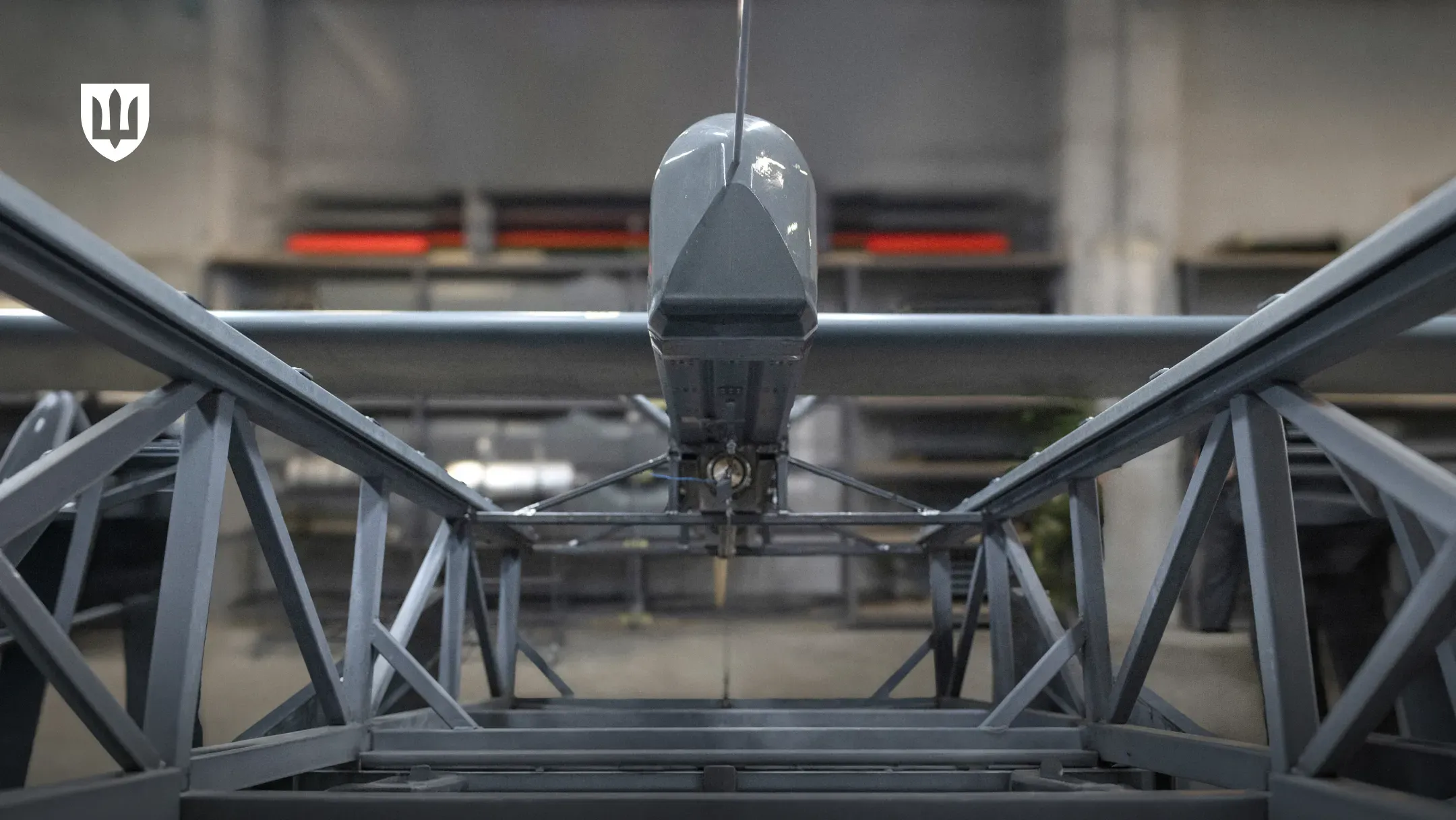 Front view of a gray fixed-wing drone mounted on a metal frame in a production facility
