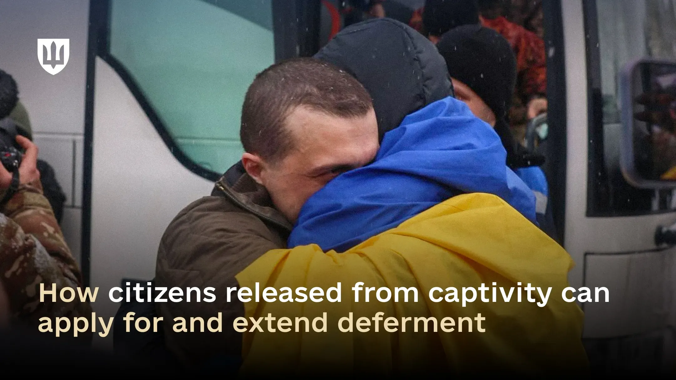 A Ukrainian man released from captivity embraces a loved one after returning, with a bus visible in the background during a prisoner exchange.