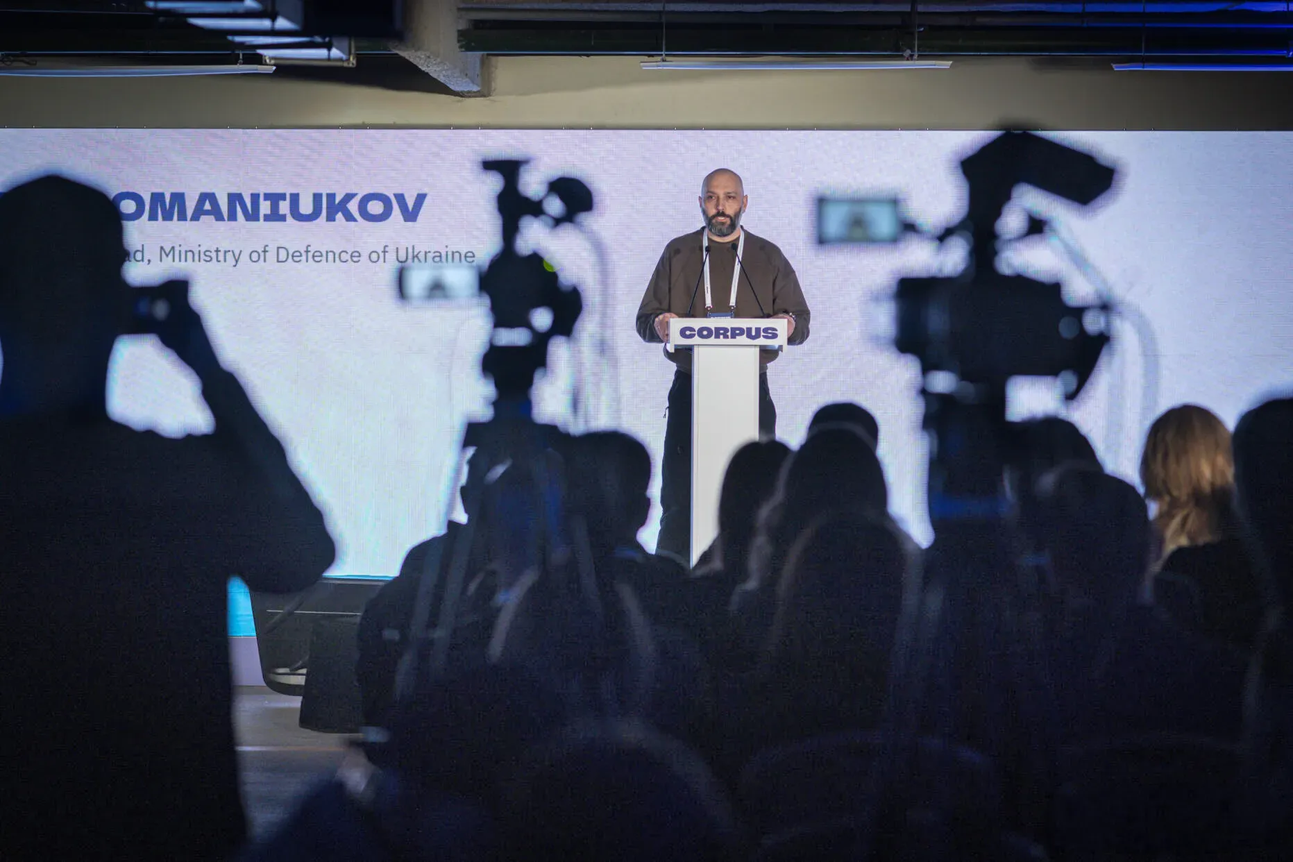 Представник Міністерства оборони України стоїть за трибуною на сцені. Його знімають відеокамери