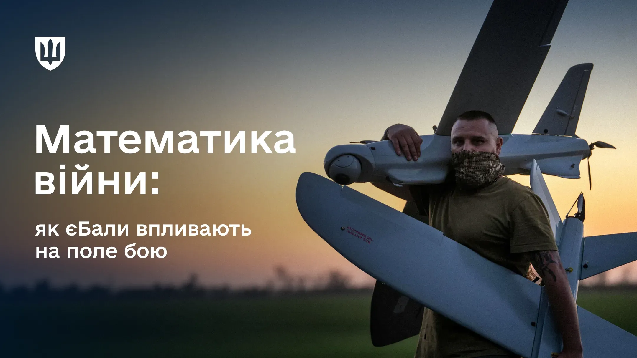 Український військовий у камуфляжній масці тримає на плечі великий безпілотник літакового типу на фоні вечірнього неба