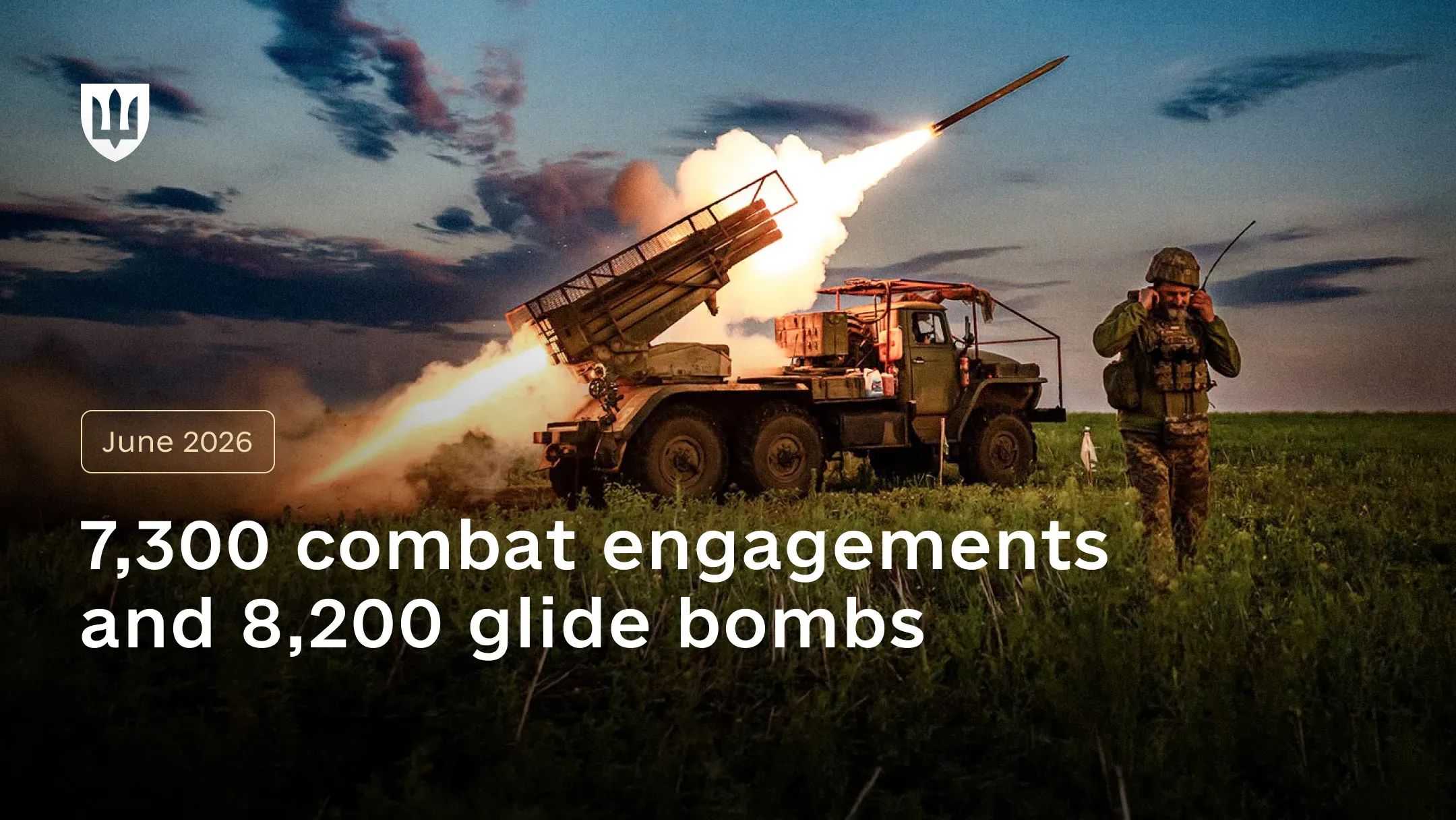A multiple launch rocket system firing a rocket in a field against the evening sky, with a service member standing nearby