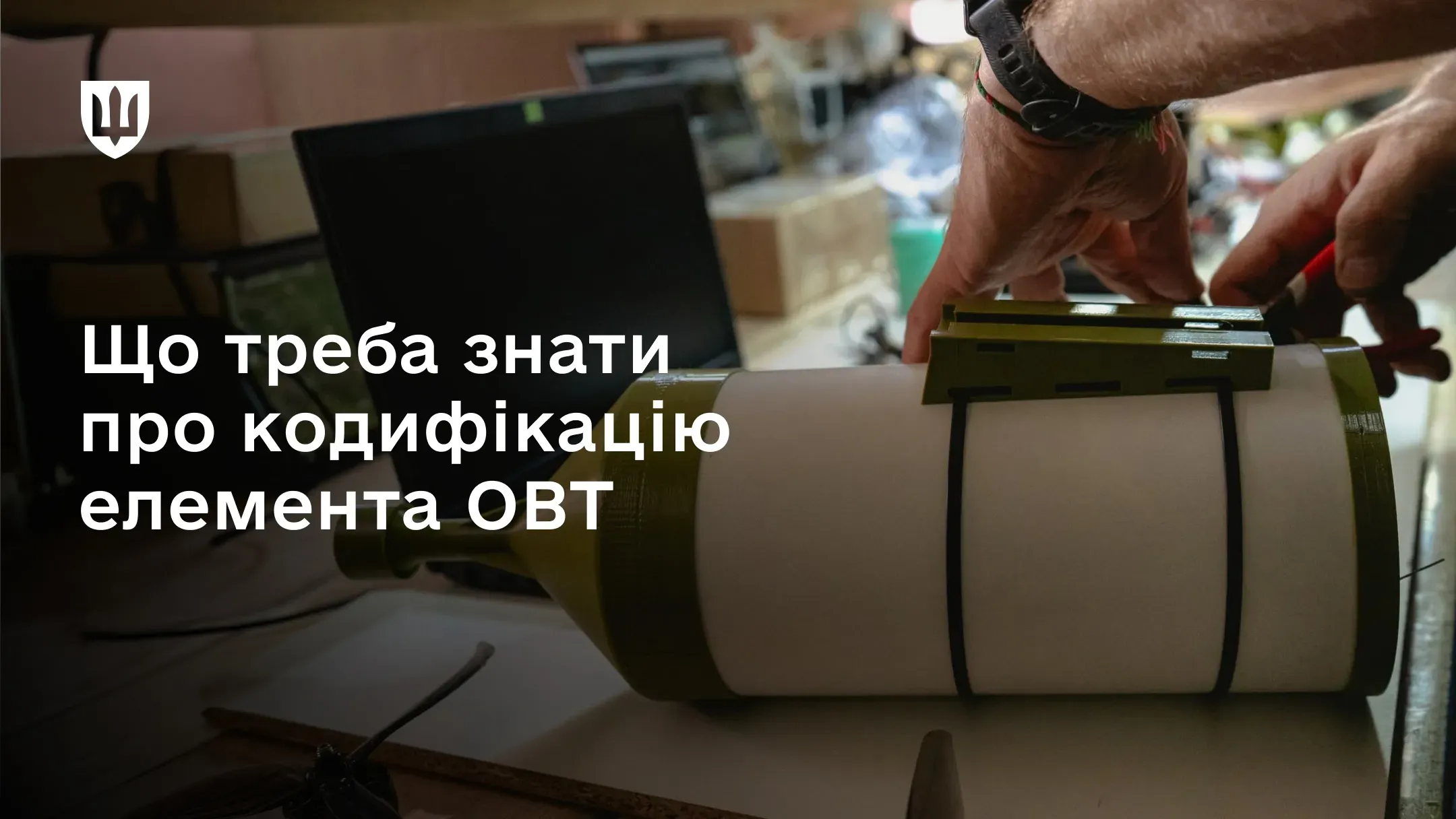 Руки фахівця працюють над елементом озброєння на робочому столі поруч із ноутбуком
