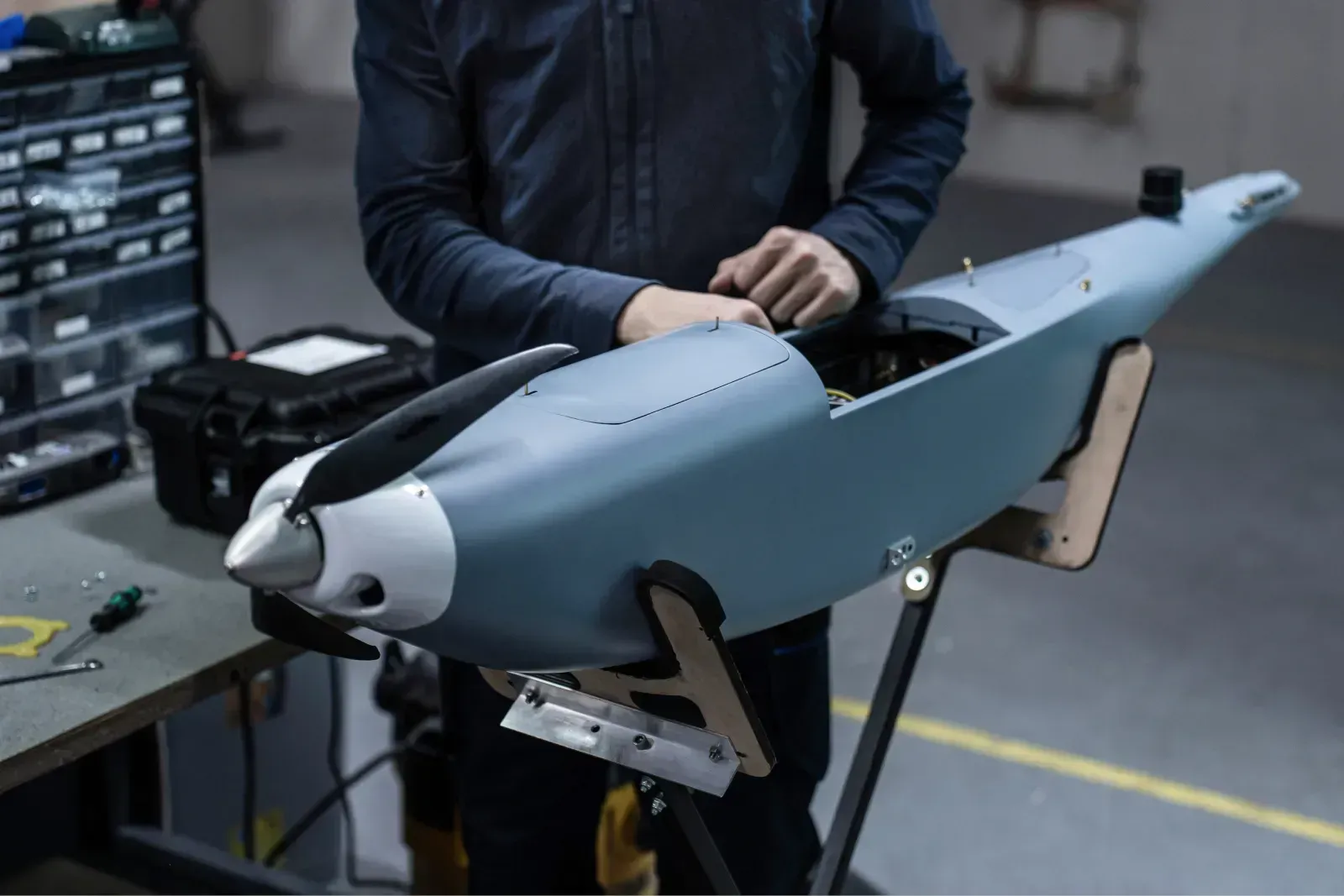 A person assembles a fixed-wing unmanned aerial vehicle with a front-mounted propeller on a stand in a workshop