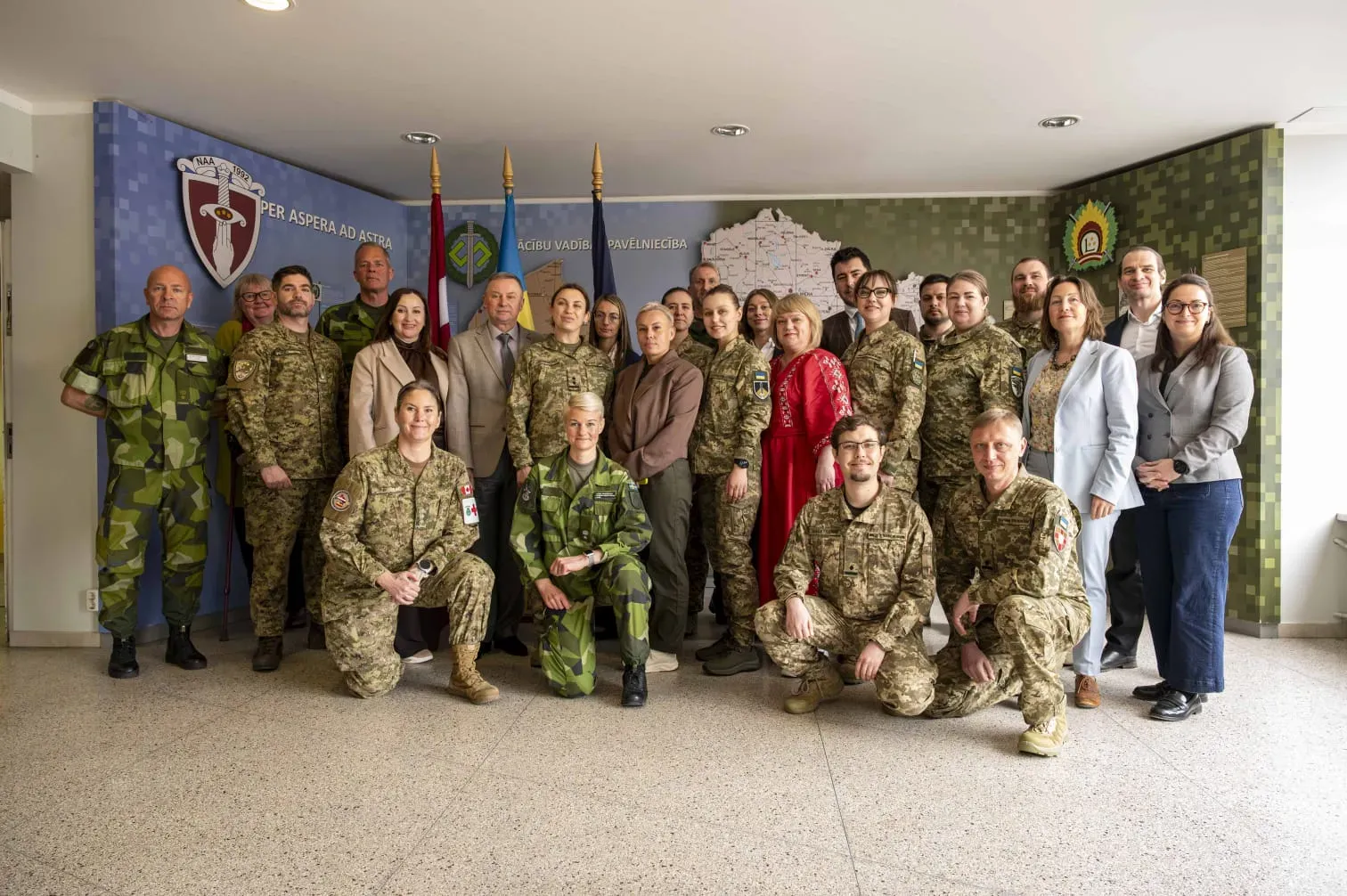 Група жінок та чоловіків, частина яких у військовій формі України та країн НАТО позує на фоні прапорів України, Латвії та НАТО
