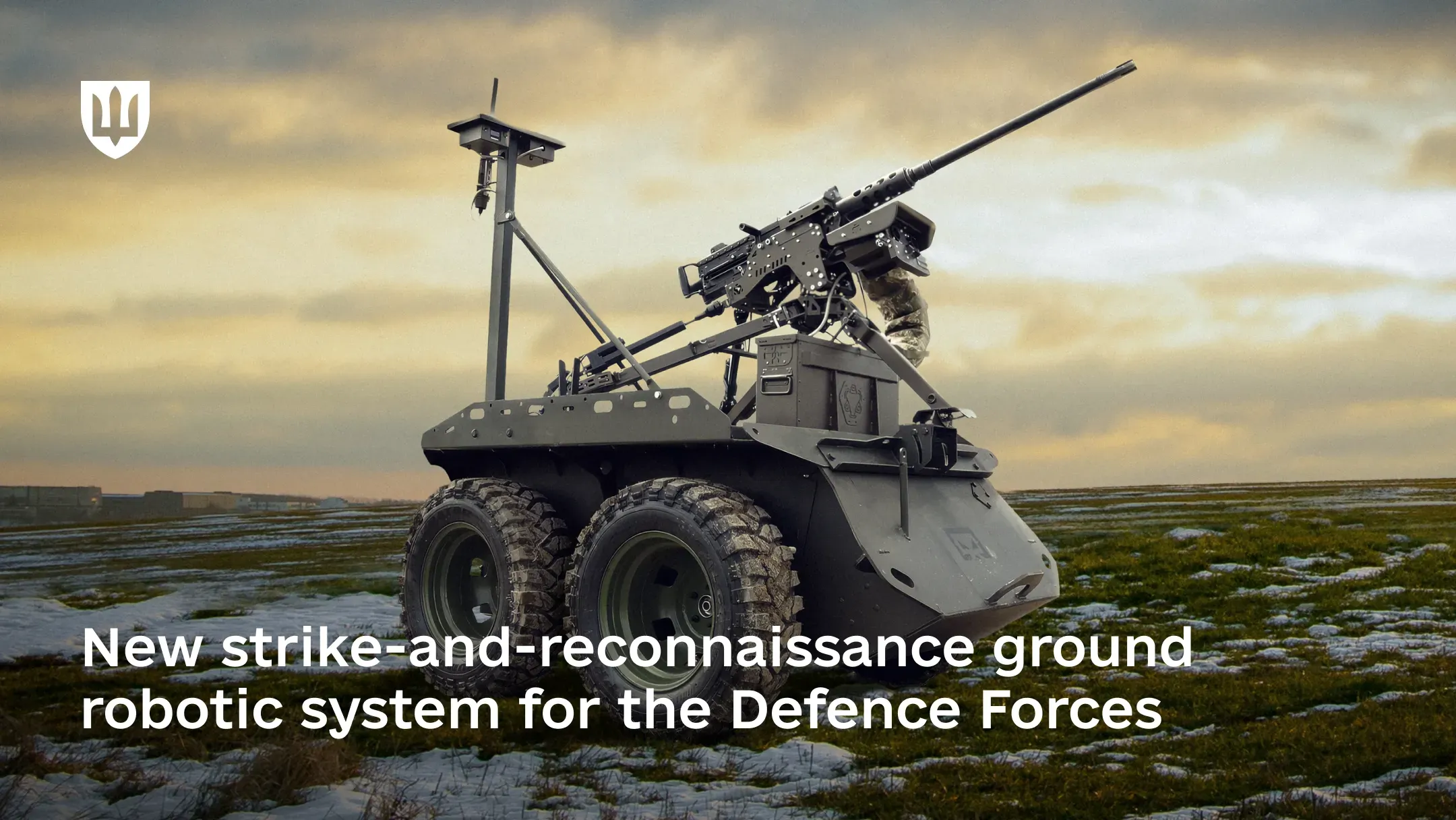 A dark olive–colored Zmiy Droid 12.7 ground drone with large off-road tires stands in open terrain, equipped with a turret-mounted automatic weapon covered by a camouflage cover and an antenna